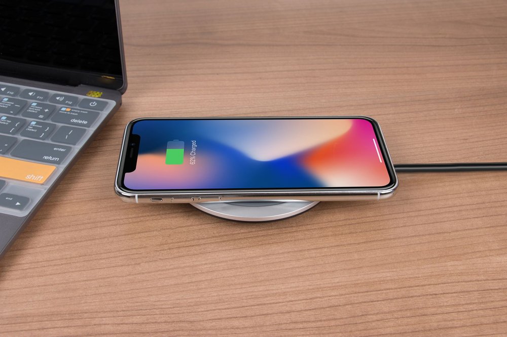 iPhone ładujący się bezprzewodowo na biurku obok laptopa