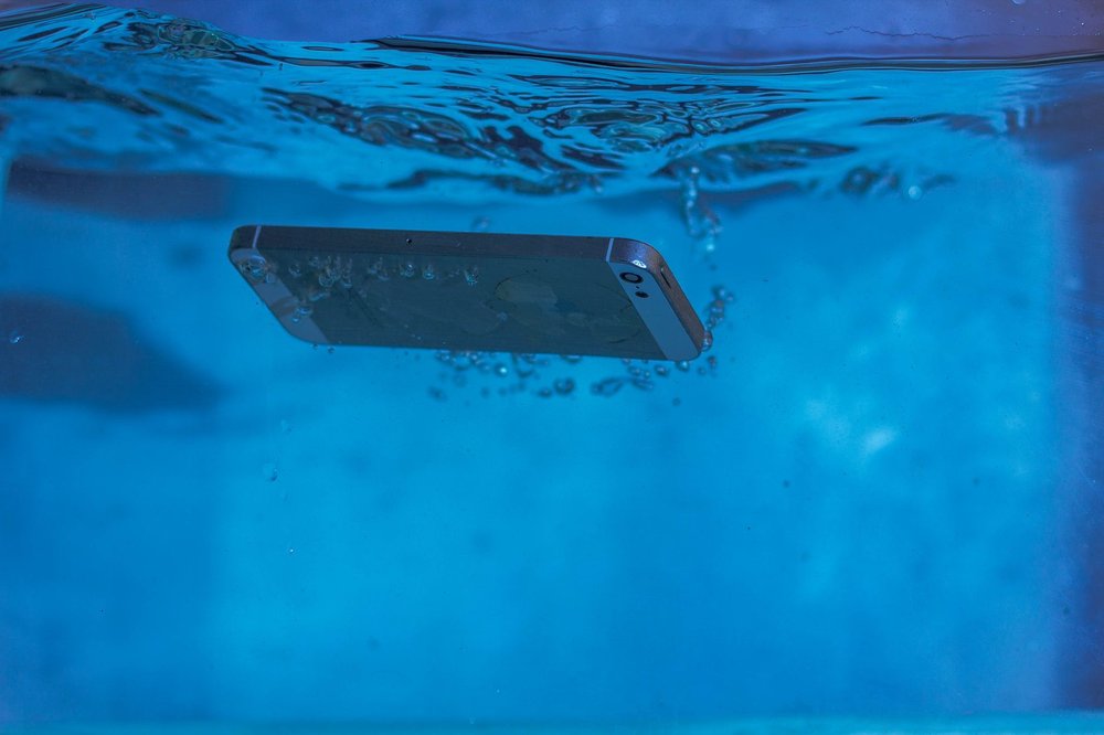 Smartfon pod wodą z bąbelkami powietrza w błękitnej wodzie