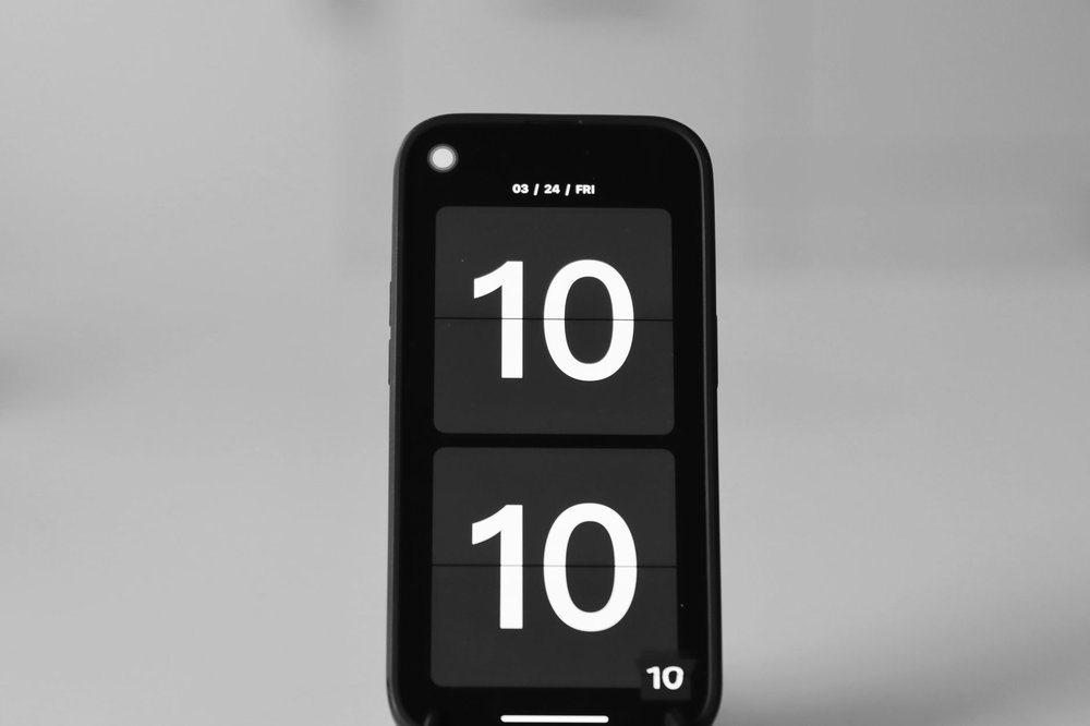 Zbliżenie na ekran iPhone'a z cyfrowym budzikiem o godzinie 10:10